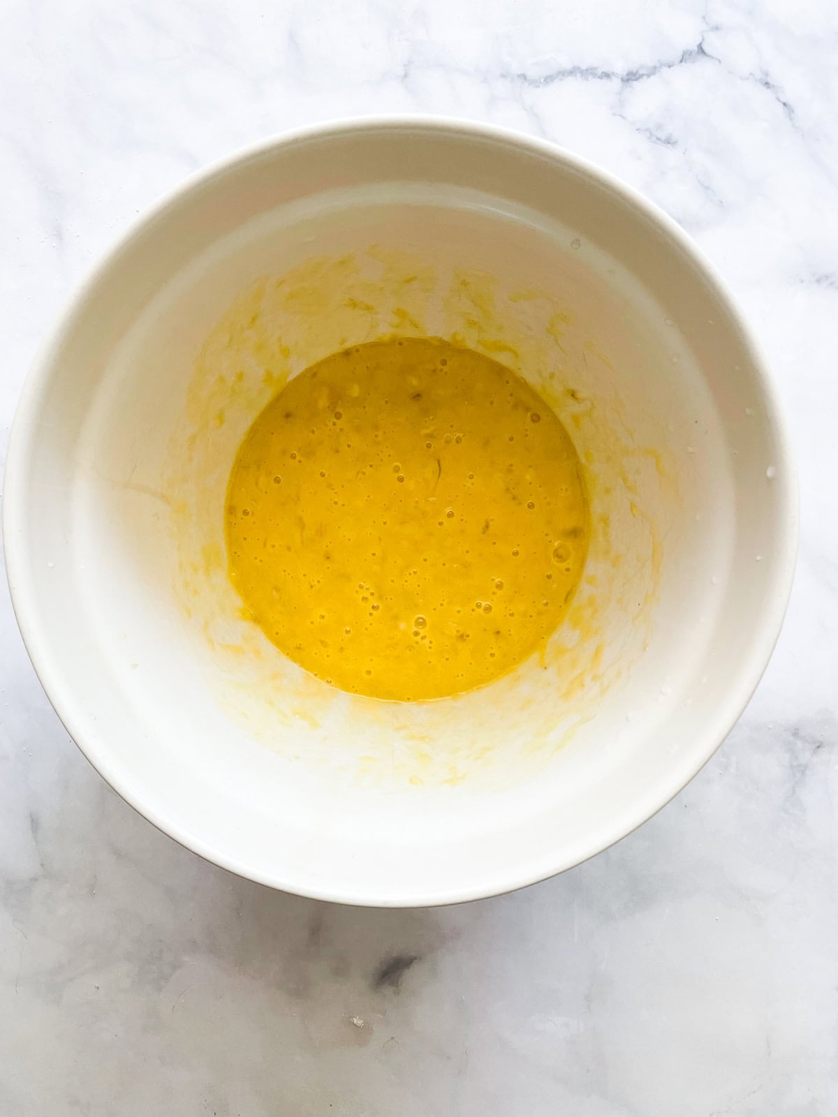 This recipe for gluten free coconut banana bread produces a beautiful loaf with a dense, moist crumb that's swirled with shredded coconut. Bananas are mixed with eggs and oil in a bowl.