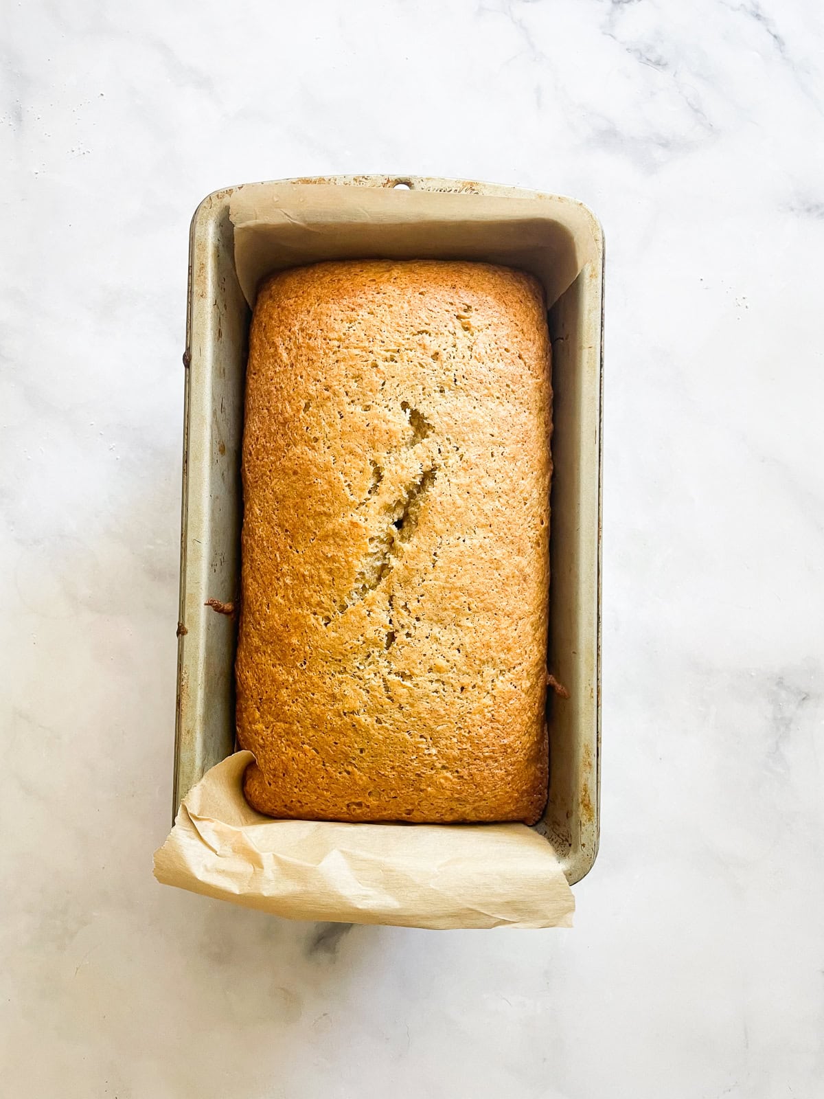 This recipe for gluten free coconut banana bread produces a beautiful loaf with a dense, moist crumb that's swirled with shredded coconut. A loaf of gluten free coconut banana bread cools in a pan.