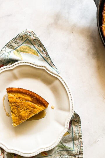 A slice of gluten free maple cornbread on a plate next to a pan of cornbread.