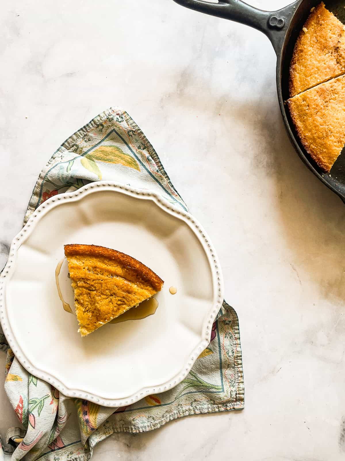 This gluten-free maple cornbread is tender-crumbed perfection thanks to buttermilk. Naturally sweetened with pure maple syrup! A slice of gluten free maple cornbread on a plate next to a pan of cornbread.