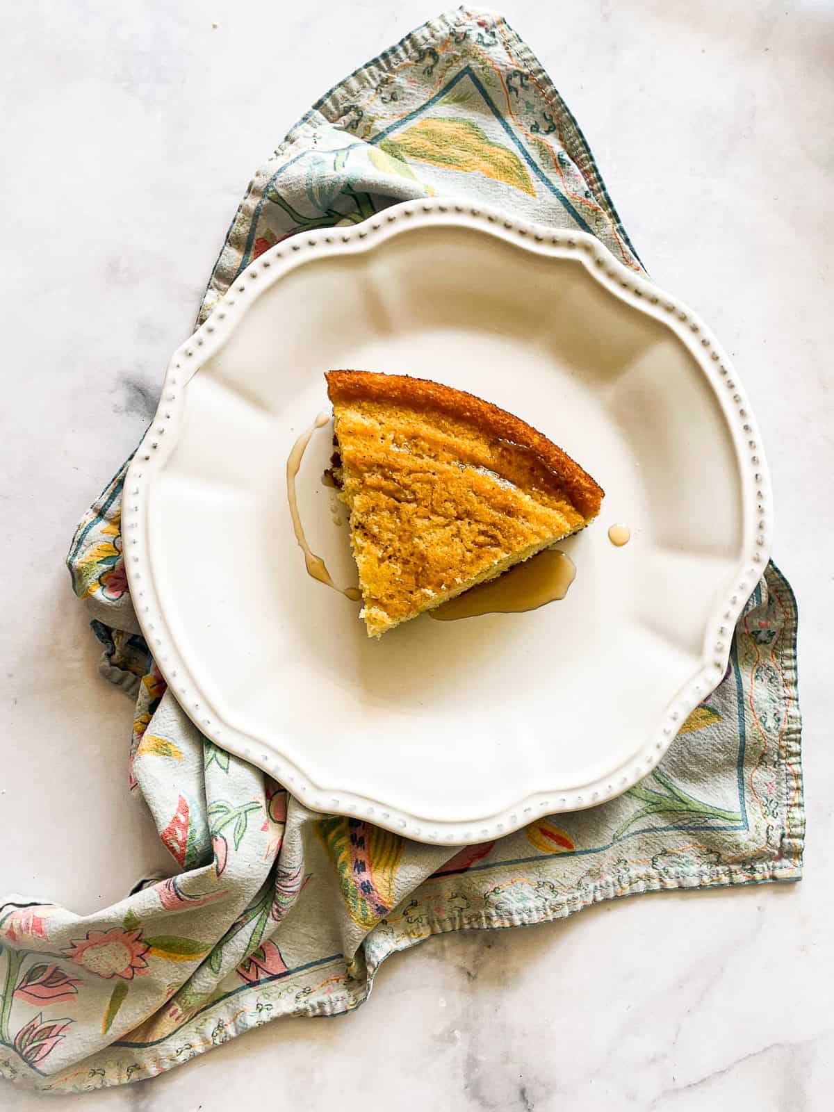 This gluten-free maple cornbread is tender-crumbed perfection thanks to buttermilk. Naturally sweetened with pure maple syrup! A plate with a slice of gluten free maple cornbread on a napkin.