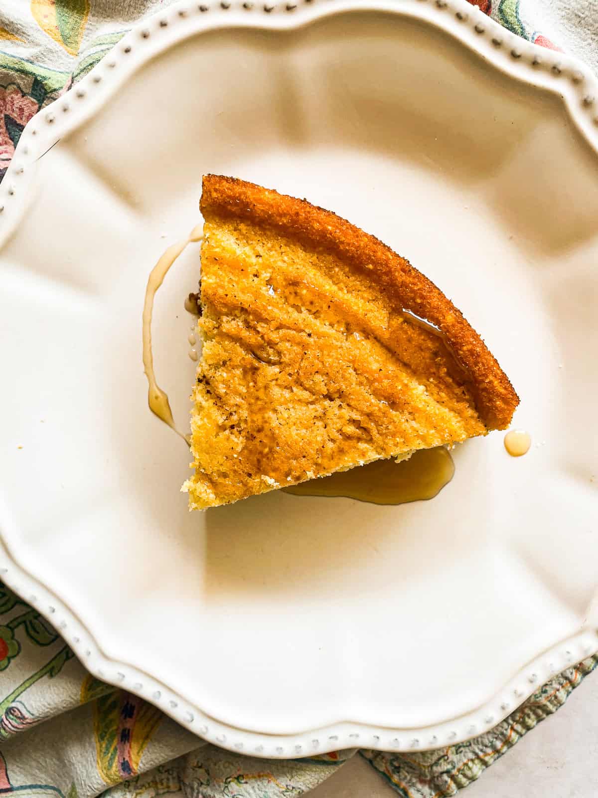This gluten-free maple cornbread is tender-crumbed perfection thanks to buttermilk. Naturally sweetened with pure maple syrup! A slice of gluten free maple cornbread topped with maple syrup on a plate.