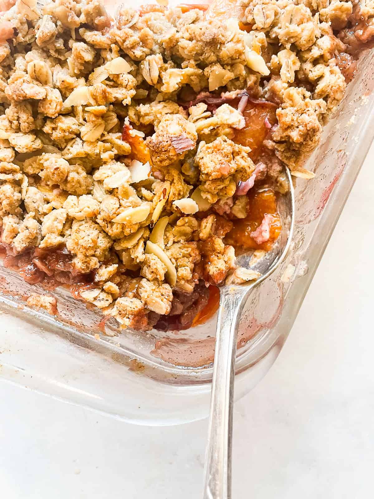 This beautifully simple gluten free nectarine crisp highlights ripe summer stone fruit. Add fresh rosemary for a lovely herbal touch. A serving spoon in a pan of gluten free nectarine crisp.