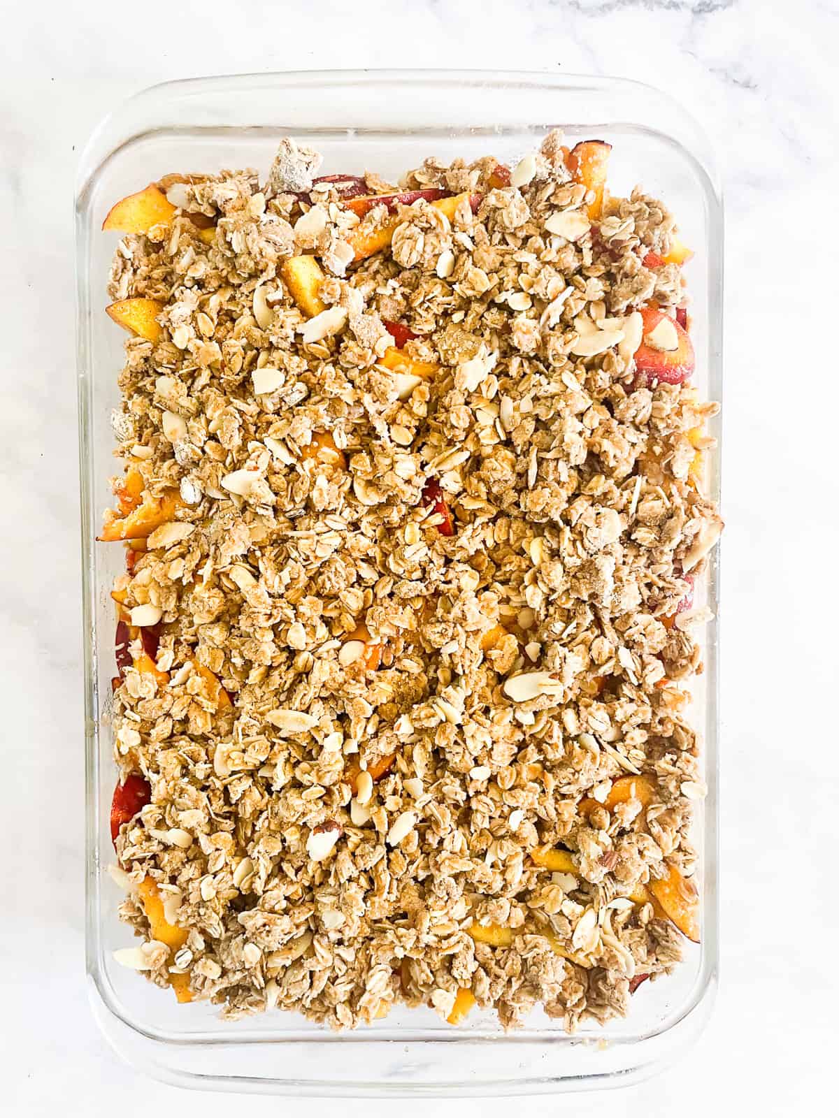 This beautifully simple gluten free nectarine crisp highlights ripe summer stone fruit. Add fresh rosemary for a lovely herbal touch. Topping is added to a pan of nectarine crisp.