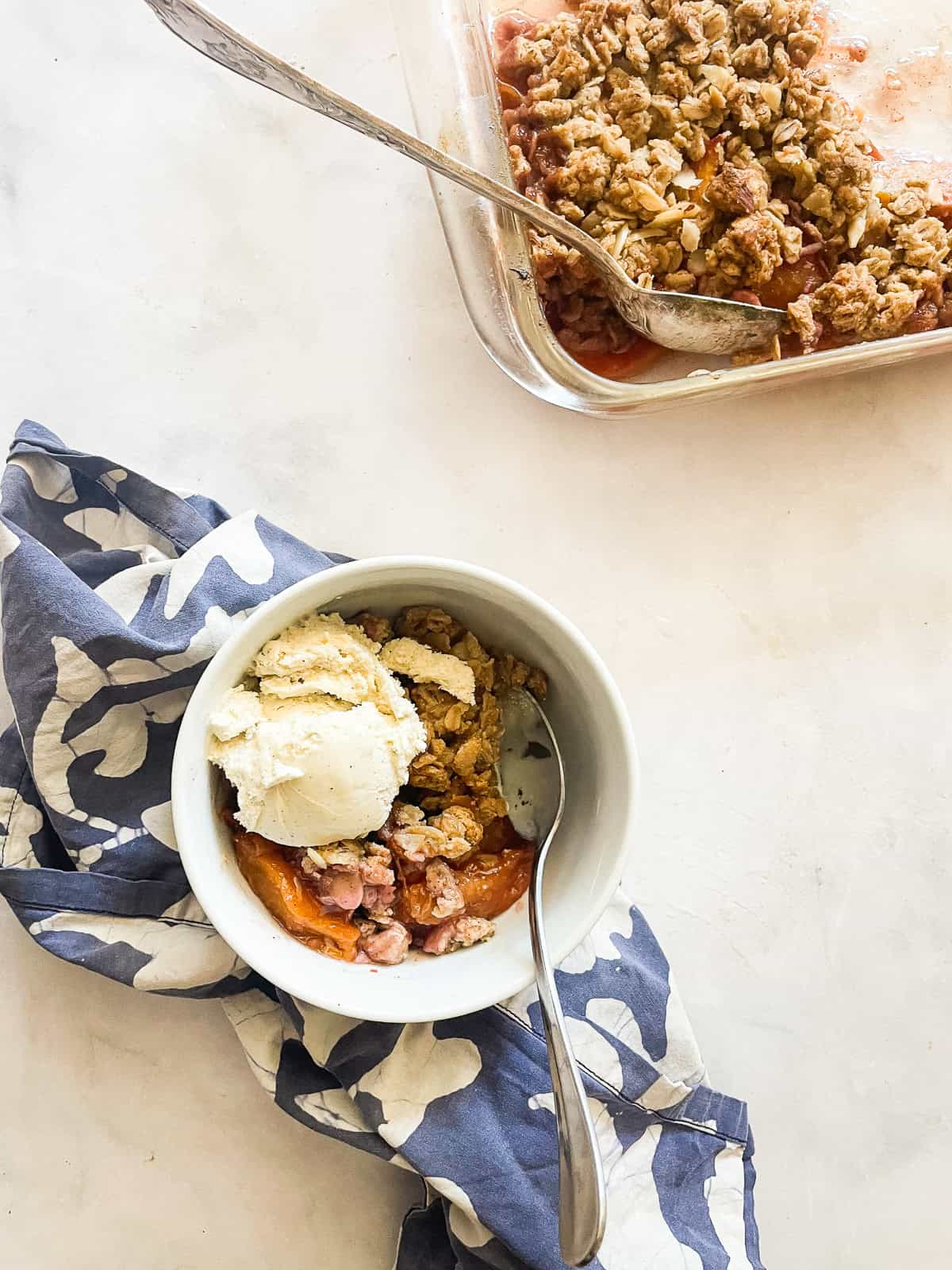 A pan of nectarine crisp next to a bowl of crisp on a napkin.