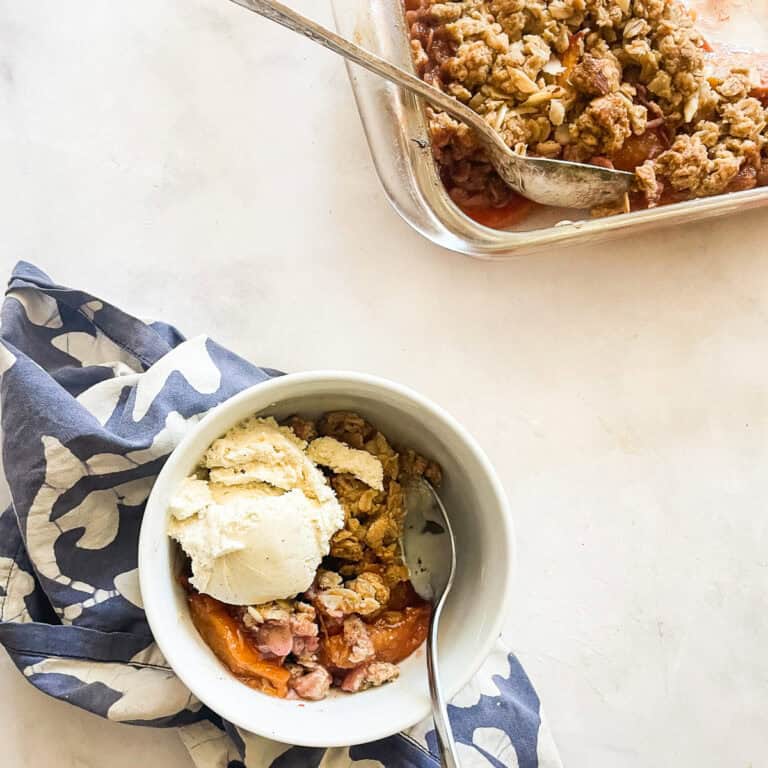 A pan of nectarine crisp next to a bowl of crisp on a napkin.