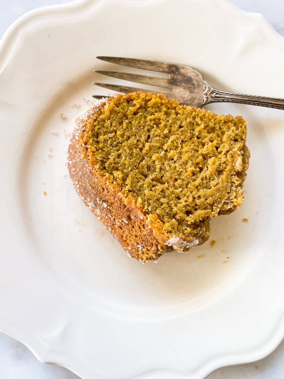 A soft and sumptuous gluten free pumpkin donut cake is bathed in cinnamon-sugar for a fabulous fall treat. A thick slice of gluten free pumpkin donut cake on a plate with a fork.
