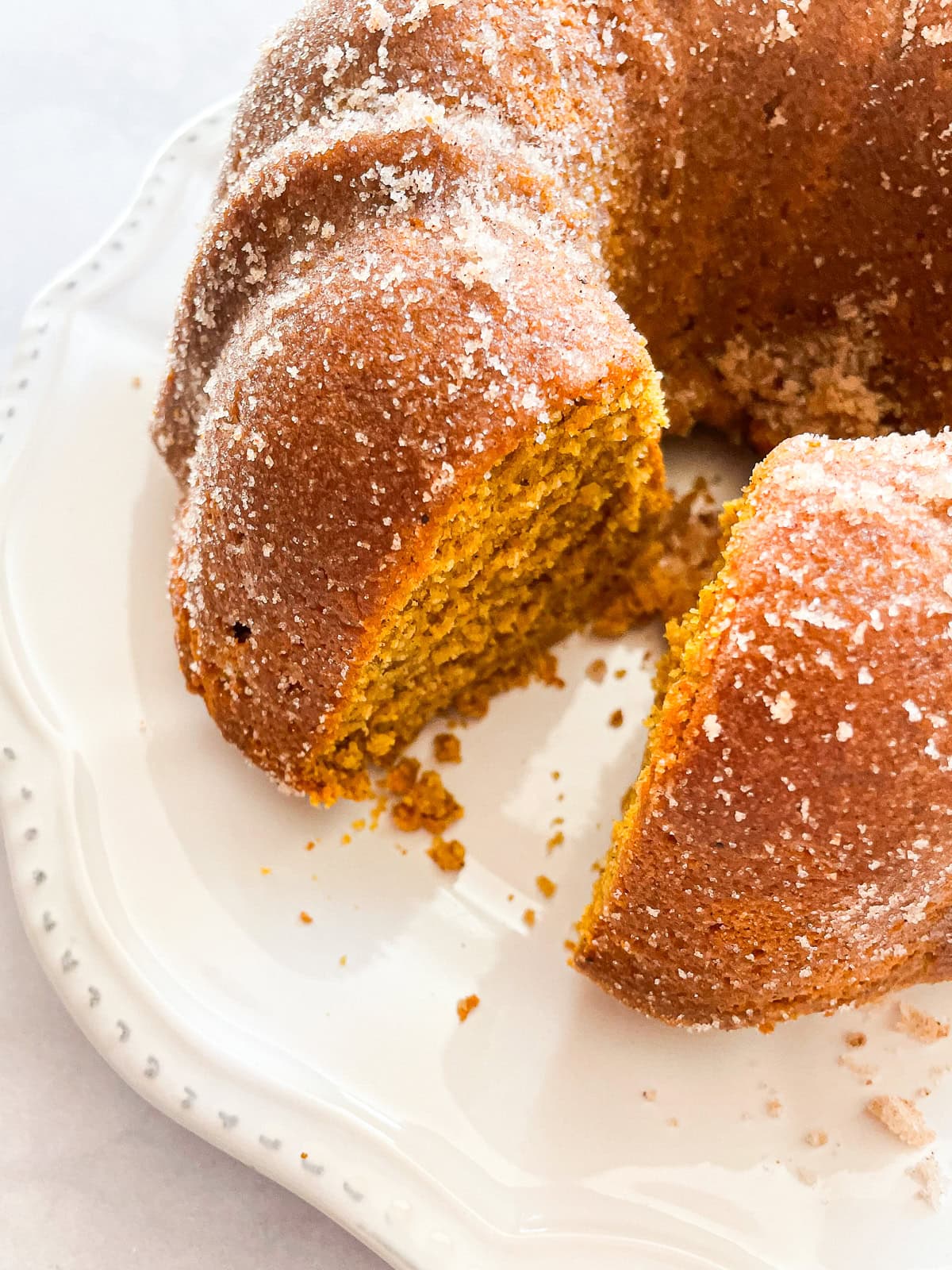 A soft and sumptuous gluten free pumpkin donut cake is bathed in cinnamon-sugar for a fabulous fall treat. A gluten free pumpkin donut cake with a slice cut out.