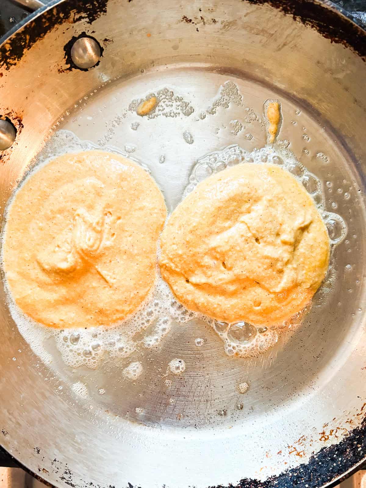 Soft and fluffy gluten free pumpkin pancakes are packed with plenty of fall flavor thanks to pumpkin puree, warming spices, and maple syrup! Two pumpkin pancakes cook in a skillet.