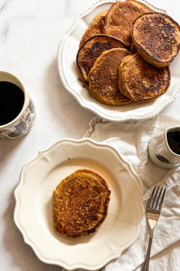 A pitcher of maple syrup and gluten free pumpkin pancakes and a cup of coffee.