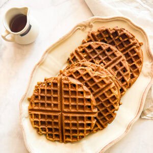 A serving dish of pumpkin waffles and a pitcher of maple syrup.