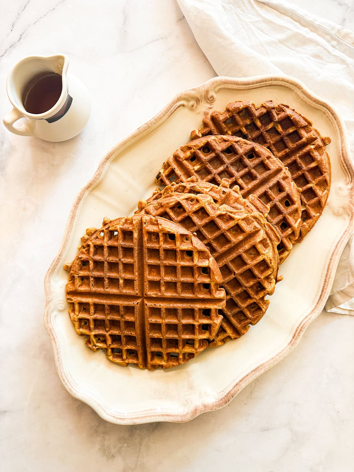 Warmly spiced and naturally gluten-free pumpkin waffles are what you want on a crisp fall morning. Made with whole grain oat flour! A serving dish of pumpkin waffles and a pitcher of maple syrup.