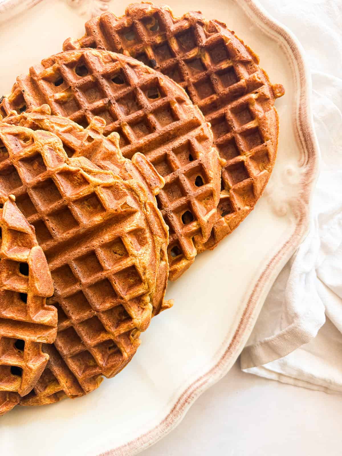 Warmly spiced and naturally gluten-free pumpkin waffles are what you want on a crisp fall morning. Made with whole grain oat flour! Spiced gluten free pumpkin waffles on a serving dish.