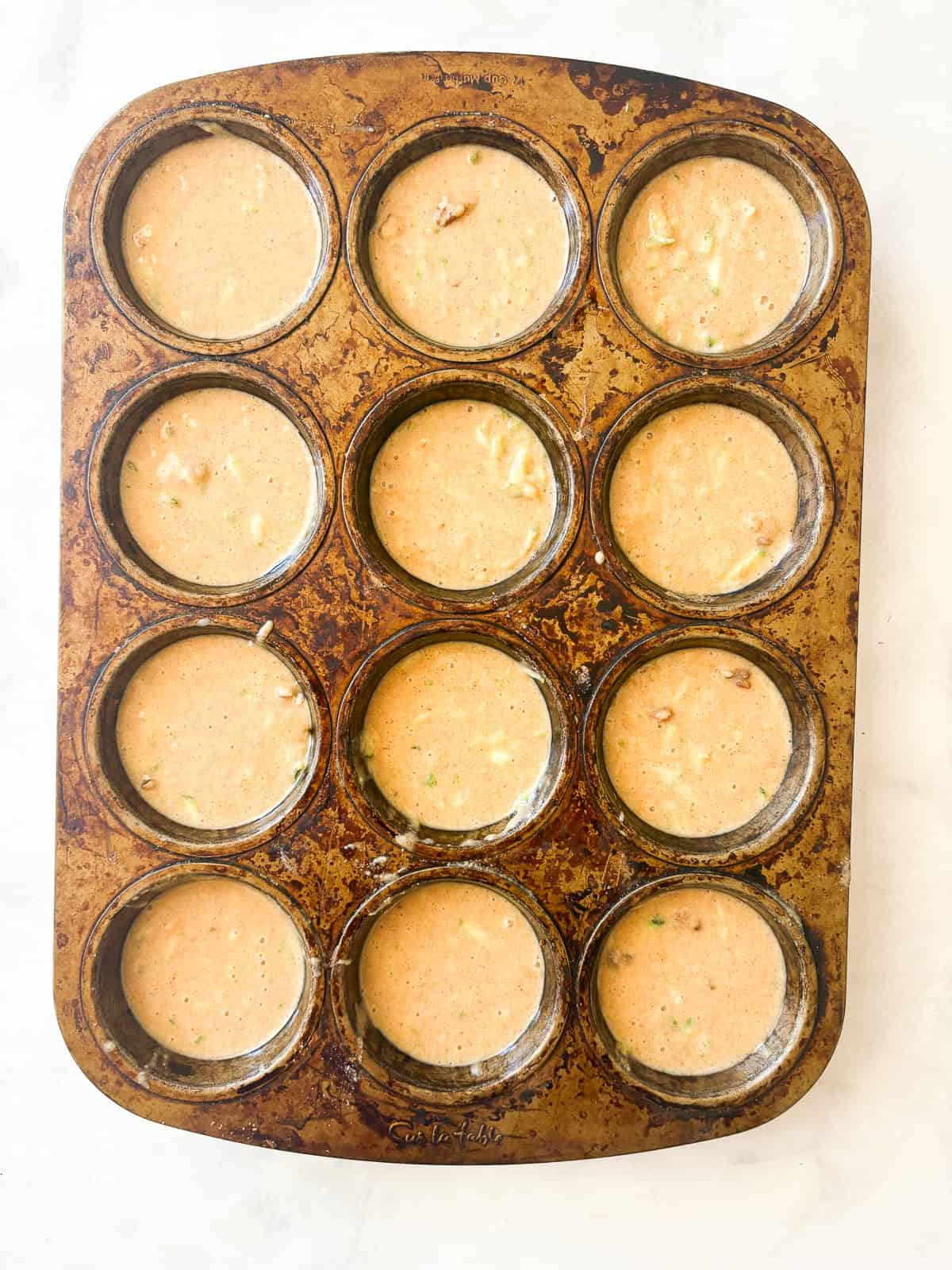 Tuck shredded squash into these gluten free zucchini chocolate chip muffins for a delectable morning treat. Muffin batter in a muffin tin.