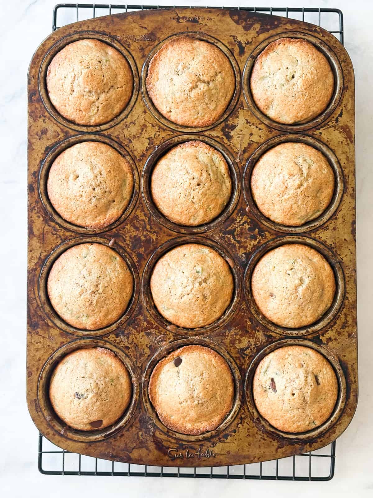 Tuck shredded squash into these gluten free zucchini chocolate chip muffins for a delectable morning treat. A batch of gluten free zucchini chocolate chip muffins cool in a tin.