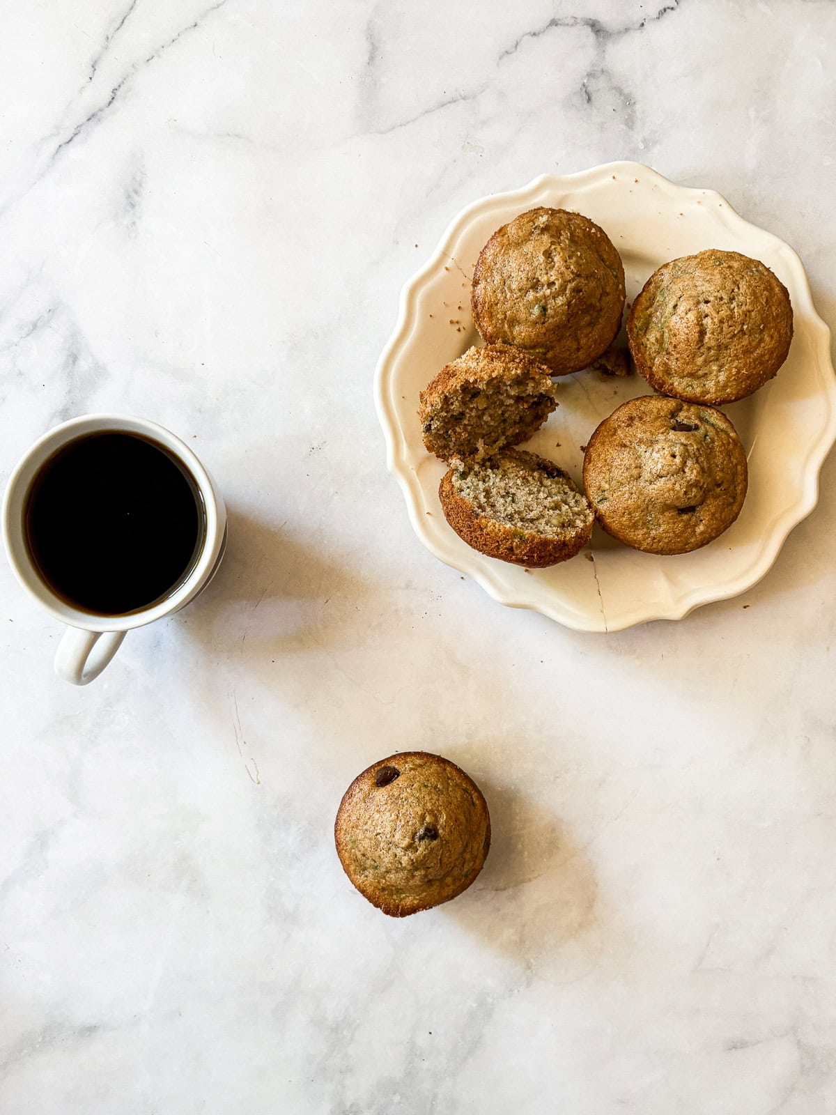 Tuck shredded squash into these gluten free zucchini chocolate chip muffins for a delectable morning treat. A plate of gluten free zucchini chocolate chip muffins and a cup of coffee plus a solo muffin.