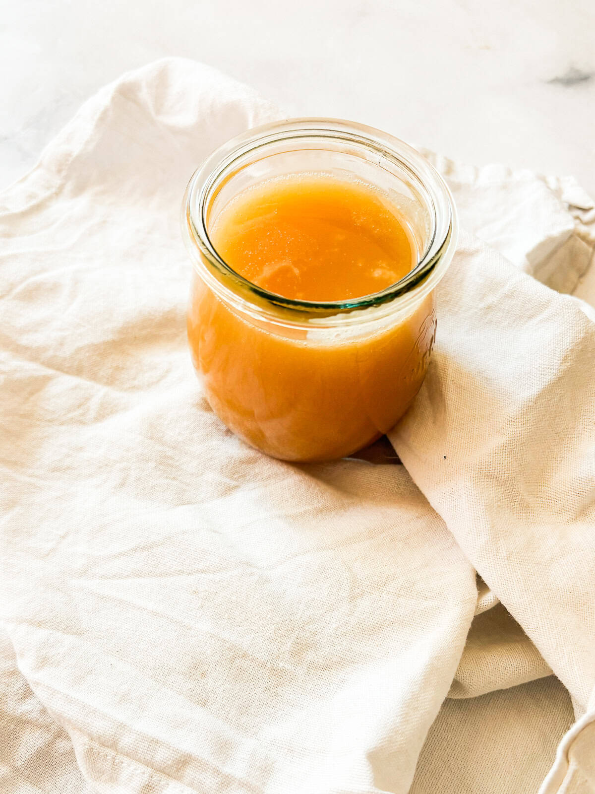 Silky and rich, this homemade salted caramel sauce is an absolute dream. Perfect over ice cream, waffles, cake, pancakes, and more. A glass jar of salted caramel sauce on a white napkin.