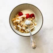 A bowl of coconut granola with yogurt and raspberries.