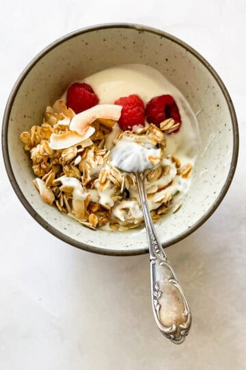 A bowl of coconut granola with yogurt and raspberries.