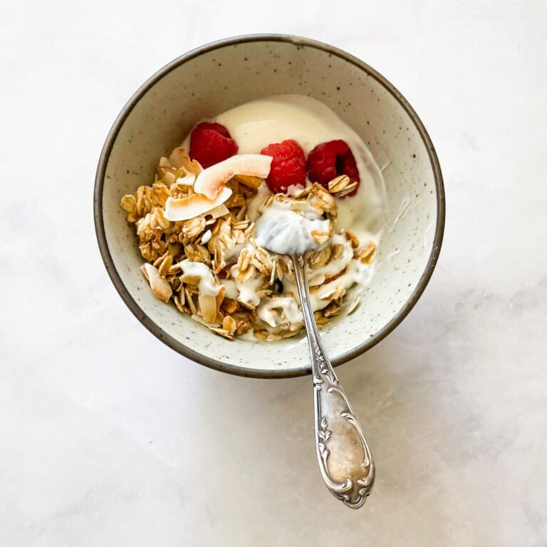 A bowl of coconut granola with yogurt and raspberries.