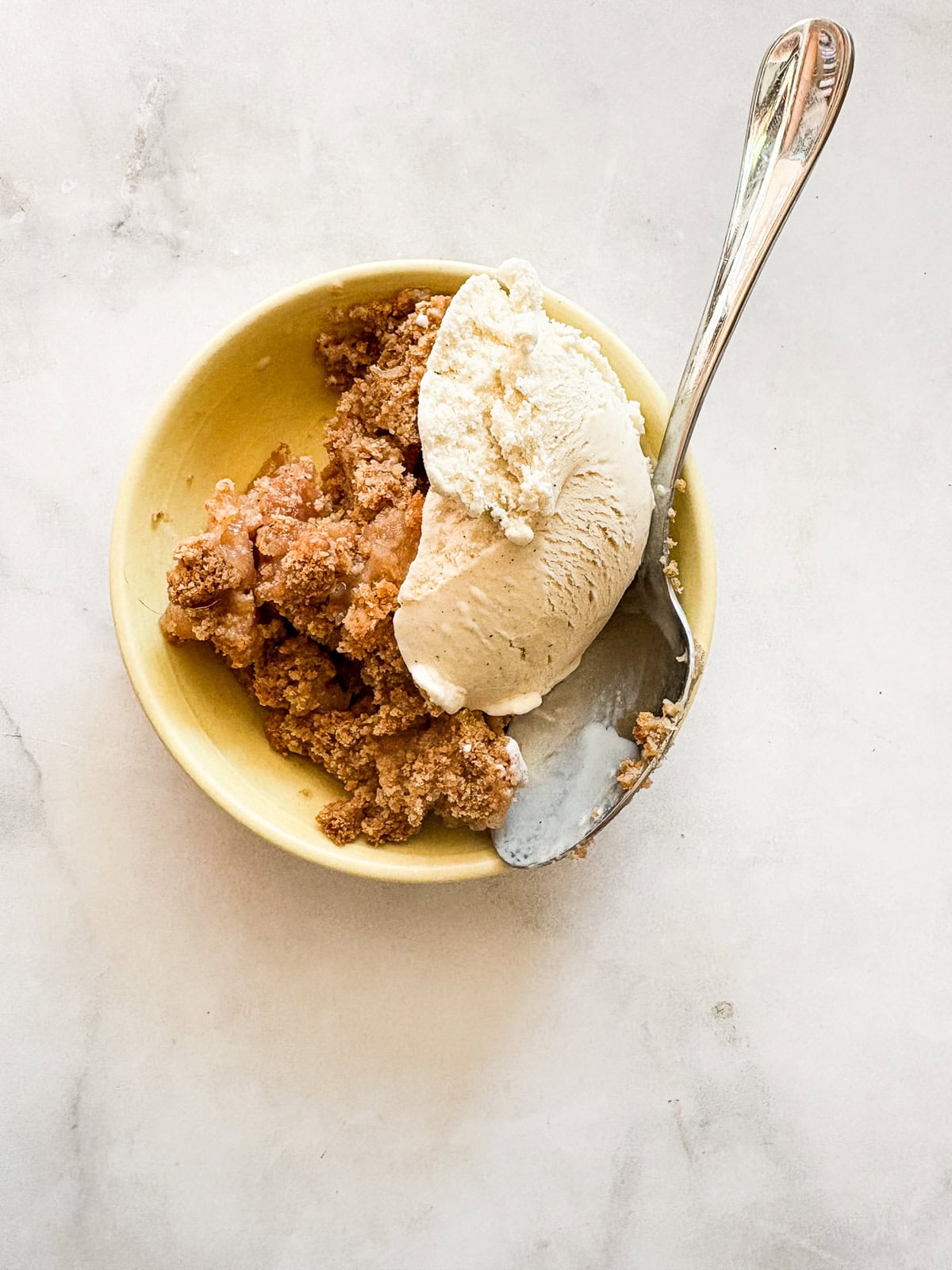 A crisp, buttery brown sugar streusel tops tender apples in this homey gluten free apple crumble. Perfect with vanilla ice cream! Vanilla ice cream tops a potion of gluten free apple crumble.