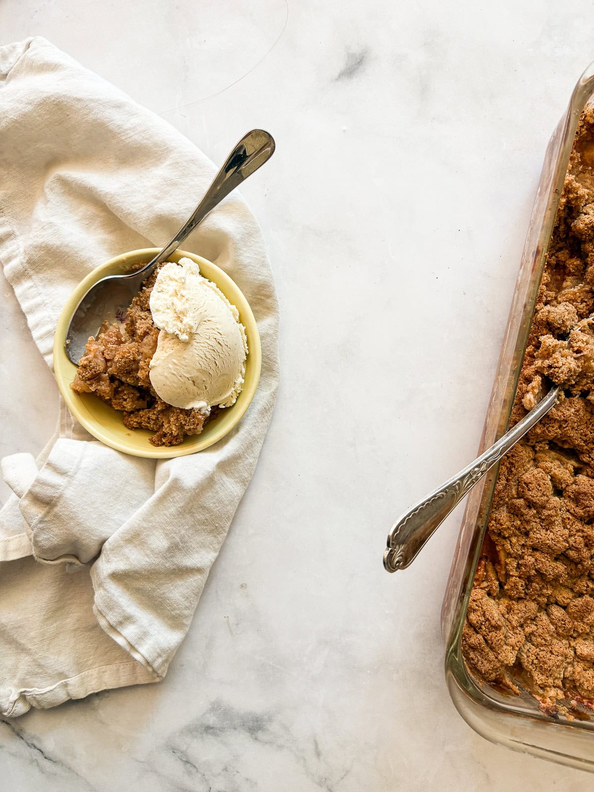 A crisp, buttery brown sugar streusel tops tender apples in this homey gluten free apple crumble. Perfect with vanilla ice cream! A bowl of gluten free apple crumble with ice cream on a napkin.