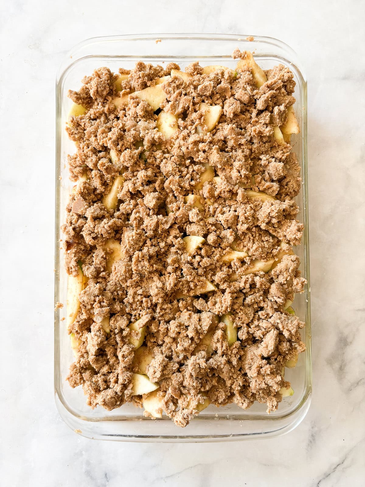 A crisp, buttery brown sugar streusel tops tender apples in this homey gluten free apple crumble. Perfect with vanilla ice cream! Topping is spread over apples in a baking dish.