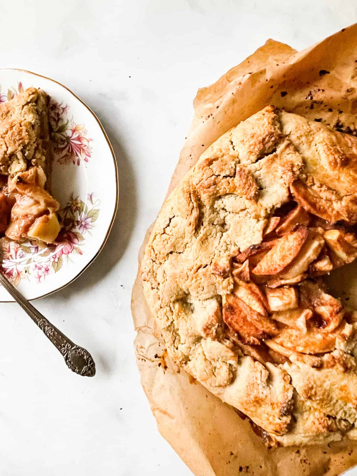 Rustic and beautiful, this gluten free apple galette wraps juicy, spiced apples in a buttery, flaky crust. Perfect for holiday gatherings! A gluten free apple galette and a slice on a plate.