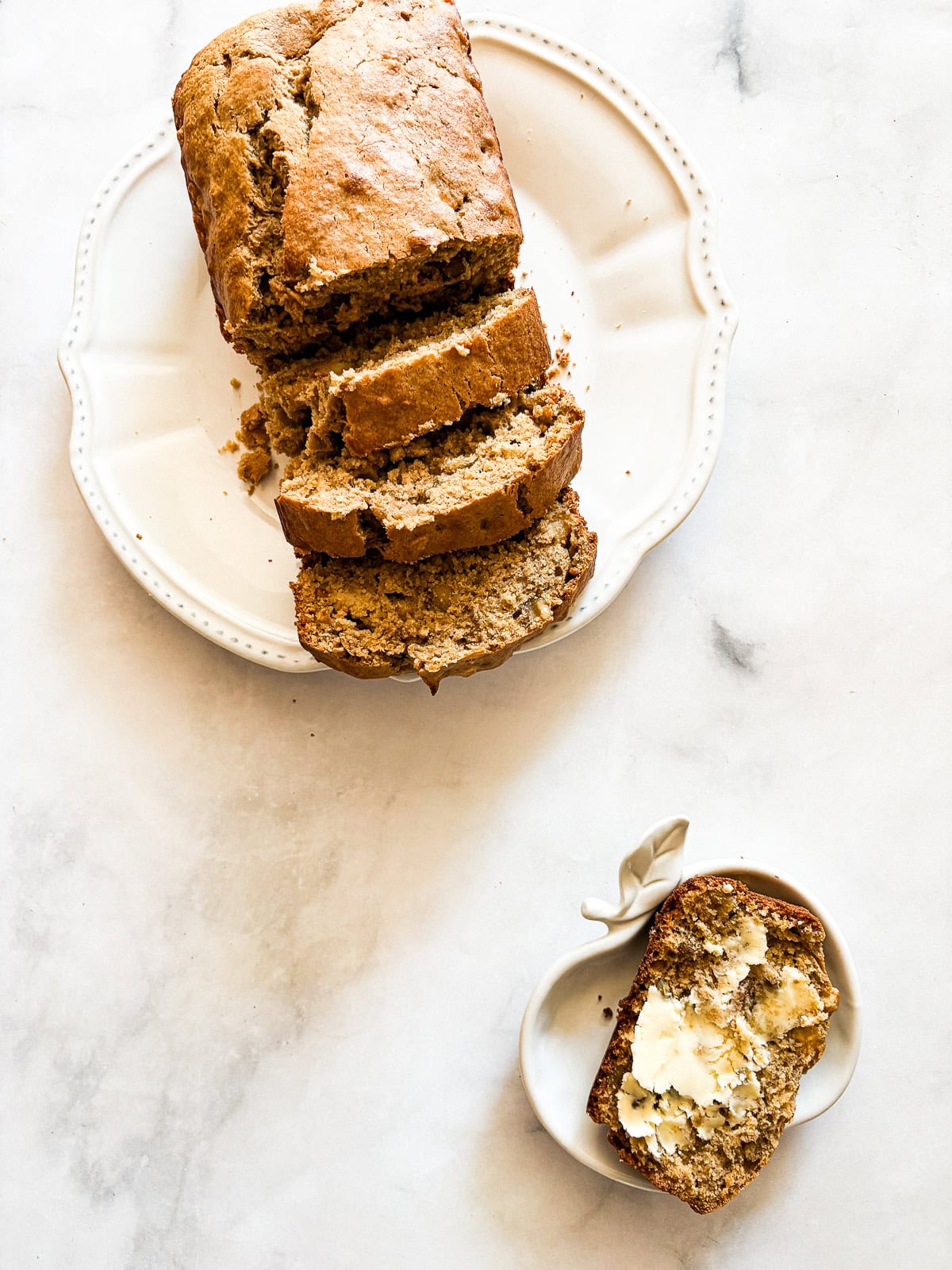 This beautifully simple yet deeply satisfying gluten free banana apple bread marries a classic banana bread with fresh for a twist. A piece of gluten free banana apple bread with butter next to a loaf.