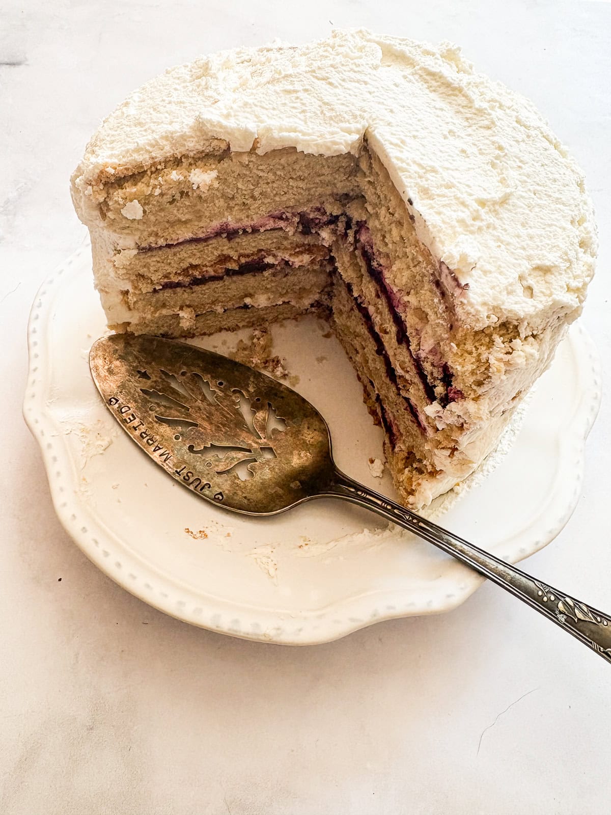 A tender gluten-free blackberry jam cake layered with whipped cream and jam that's fresh, light, and perfect for summer. A blackberry jam cake with slices removed and a cake server.