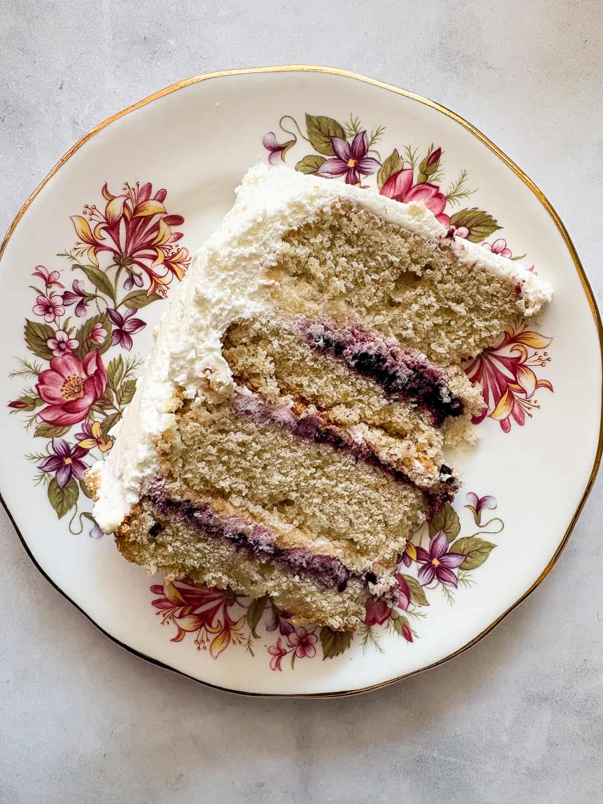 A tender gluten-free blackberry jam cake layered with whipped cream and jam that's fresh, light, and perfect for summer. A decorative plate withe a slice of gluten free blackberry jam cake.