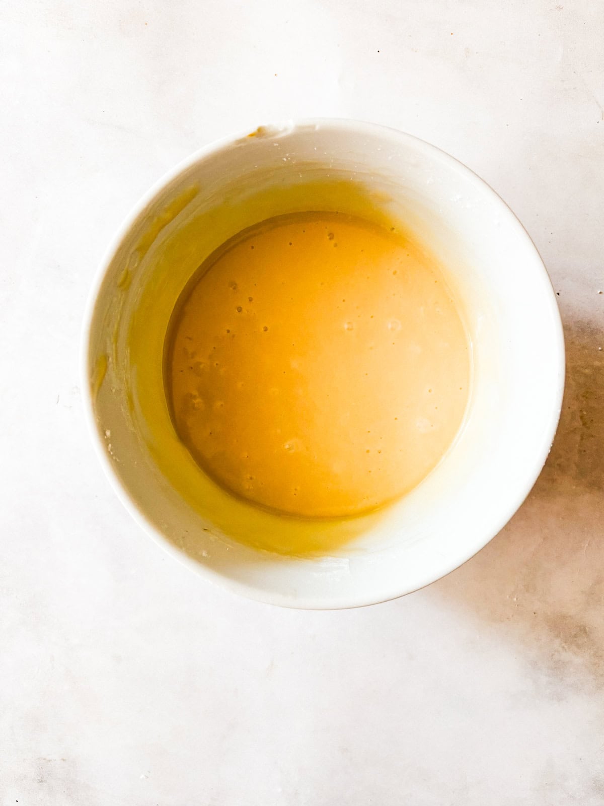 A soft, fluffy, and warmly spiced oat flour pumpkin cake that's topped with a slick of sweet maple glaze. Naturally gluten-free! The maple glaze for an oat flour pumpkin cake in a bowl.