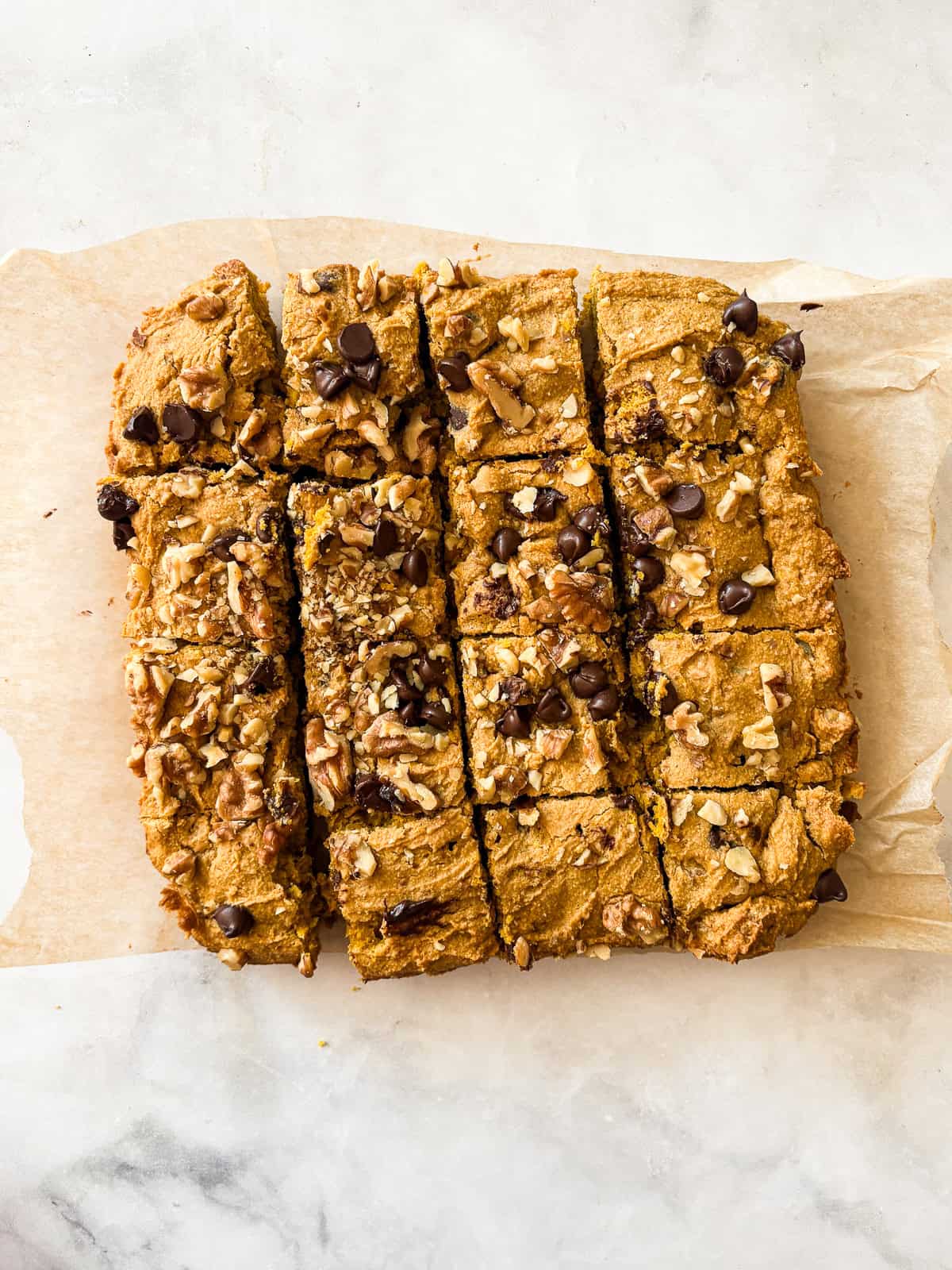 Studded with chopped walnuts and scattered with semisweet chocolate chips, gluten-free pumpkin blondies are thick and chewy. Made in 1 bowl! A batch of gluten free pumpkin blondies cut into squares.