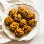 A pile of gluten free pumpkin chocolate chip cookies on a white plate on a napkin.