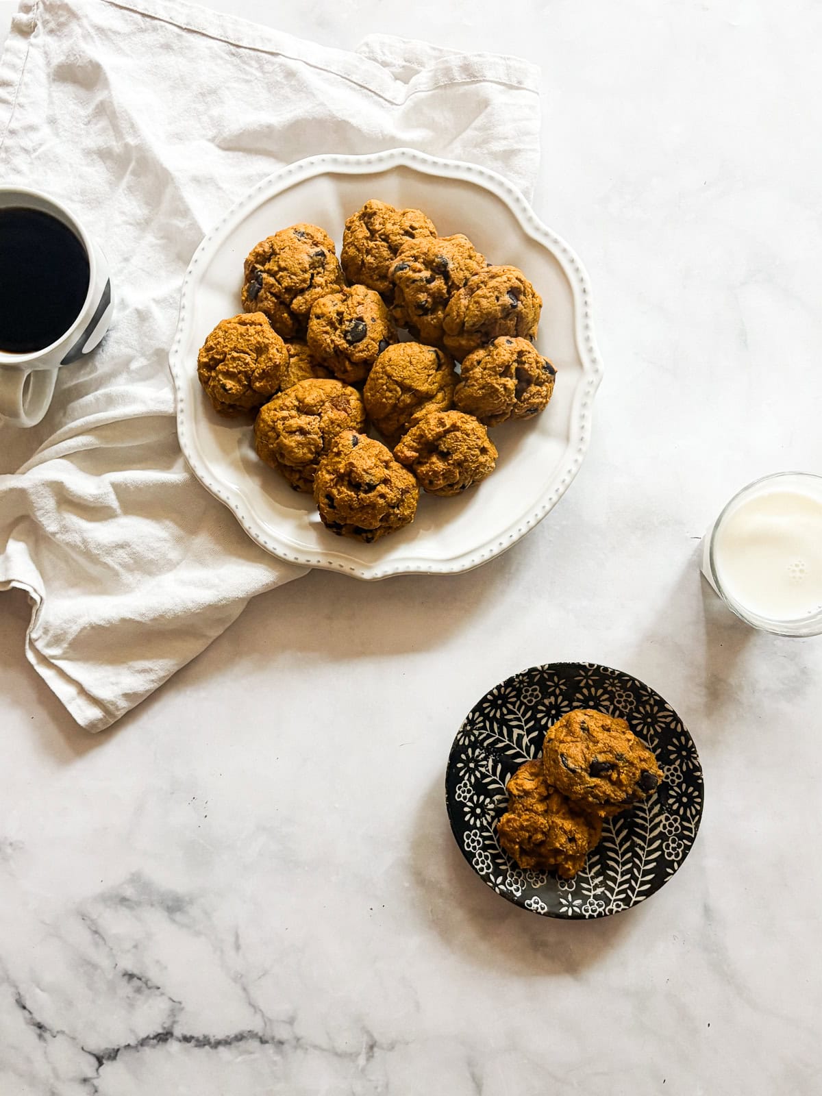 These soft-baked gluten free pumpkin chocolate chip cookies are packed with pumpkin puree, warm spices, and semisweet chocolate. A plate of gluten free pumpkin chocolate chip cookies, milk, and coffee.