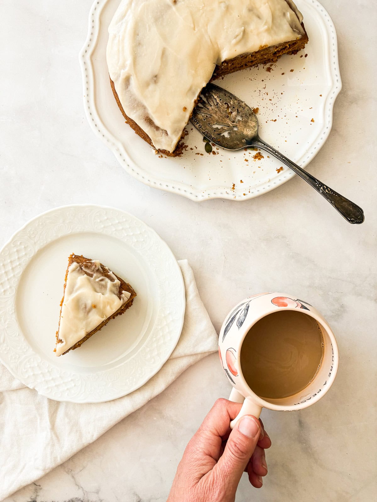 A thick maple glaze tops a soft gluten free pumpkin olive oil cake that's dairy-free, made in one bowl, and utterly delicious! Pumpkin olive oil cake with a white napkin next to a cup of coffee.