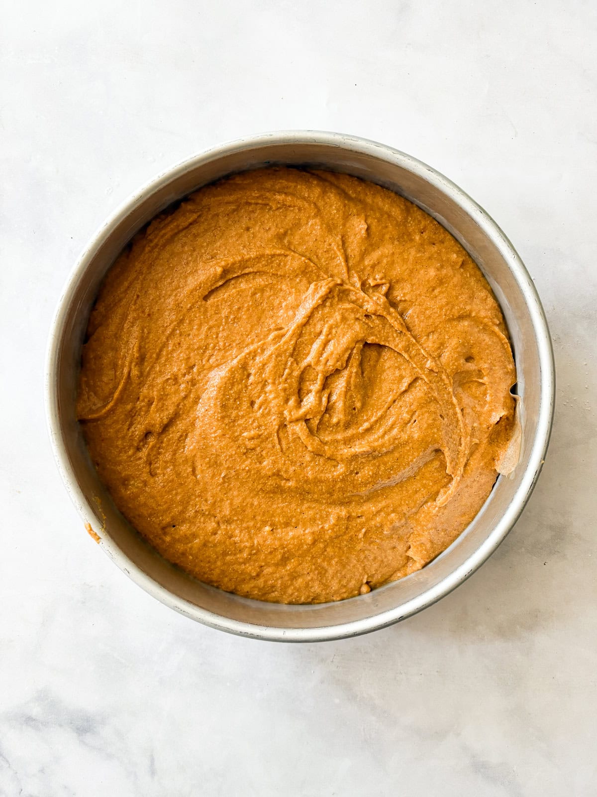 A thick maple glaze tops a soft gluten free pumpkin olive oil cake that's dairy-free, made in one bowl, and utterly delicious! Batter for pumpkin olive oil cake in a pan.