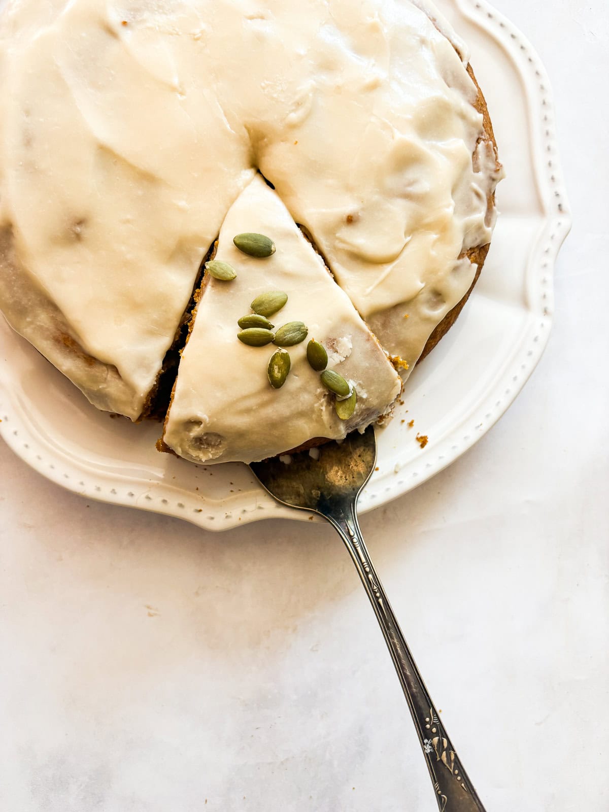 A thick maple glaze tops a soft gluten free pumpkin olive oil cake that's dairy-free, made in one bowl, and utterly delicious! A cake server lifts out a slice of pumpkin olive oil cake.