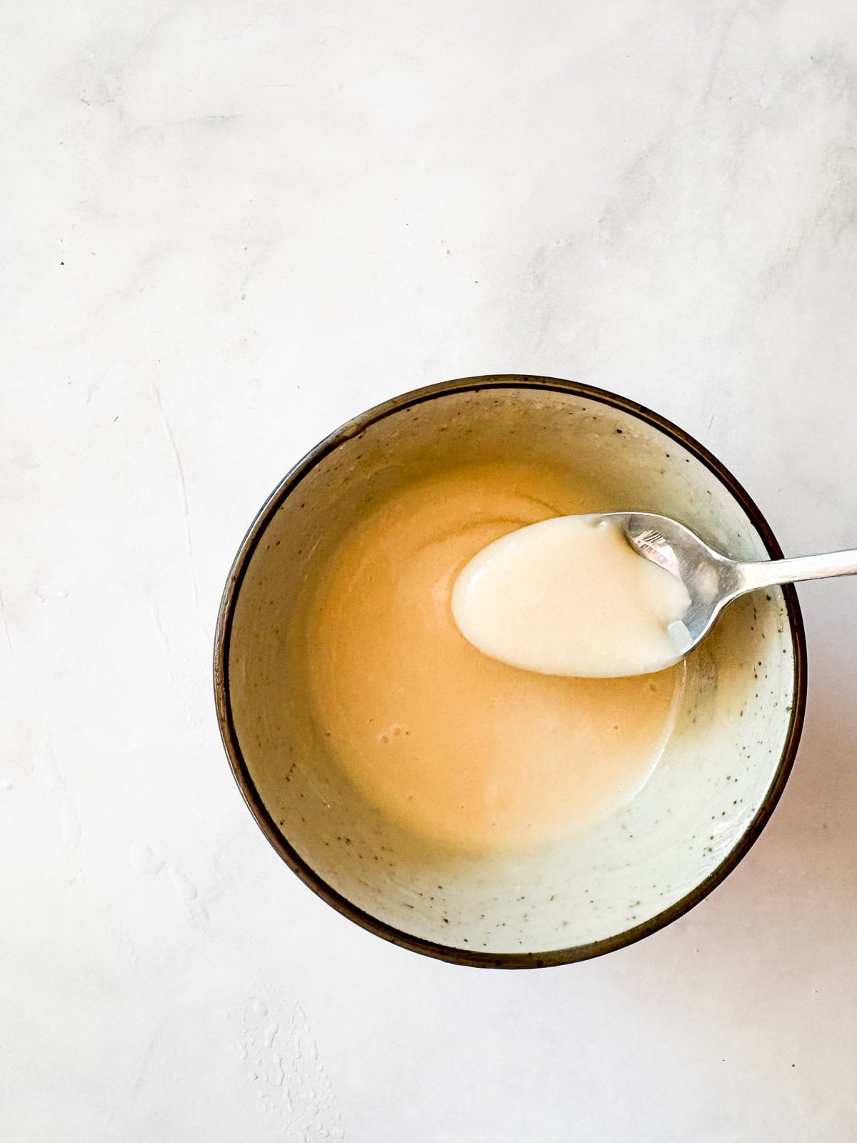 This smooth and luxurious maple glaze recipe needs just three simple ingredients to make and is wonderful on scones, pumpkin bread, and more. A spoon in a bowl of maple glaze.