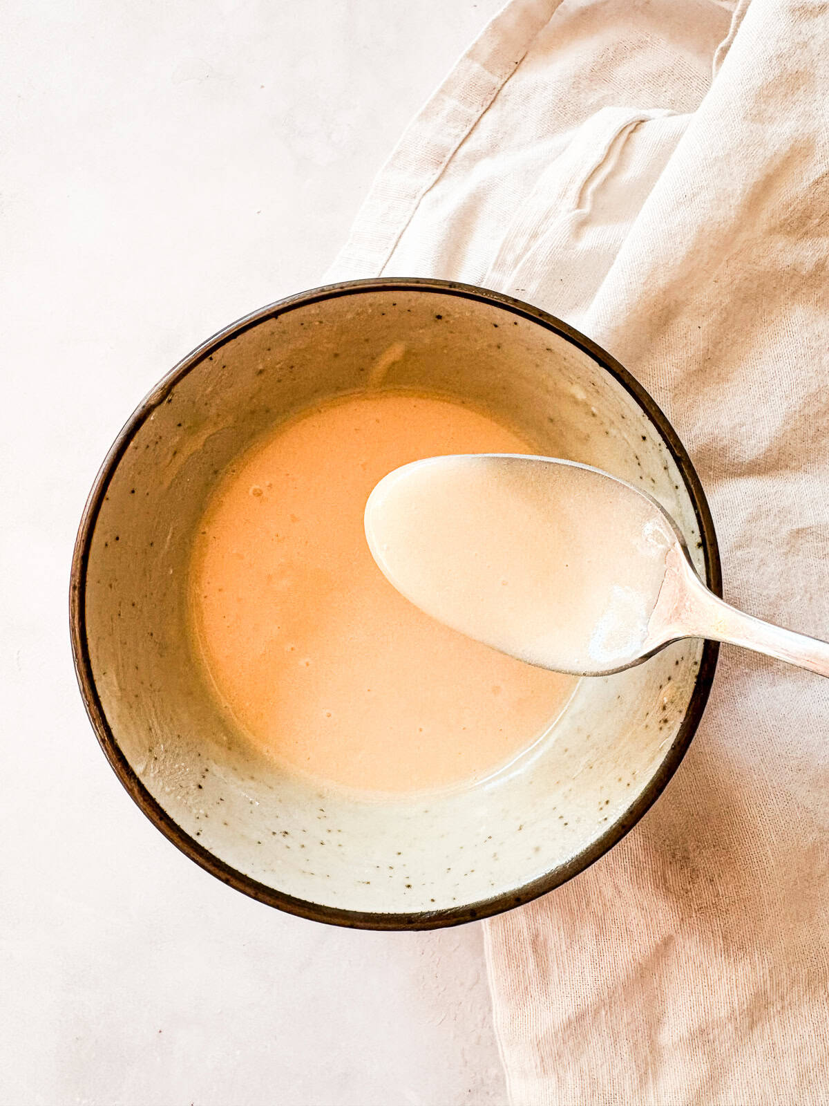 This smooth and luxurious maple glaze recipe needs just three simple ingredients to make and is wonderful on scones, pumpkin bread, and more. A spoon and a bowl of maple glaze.