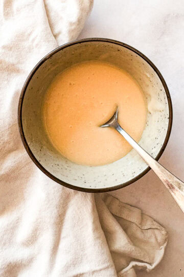 A bowl of maple glaze on a white napkin with a spoon.