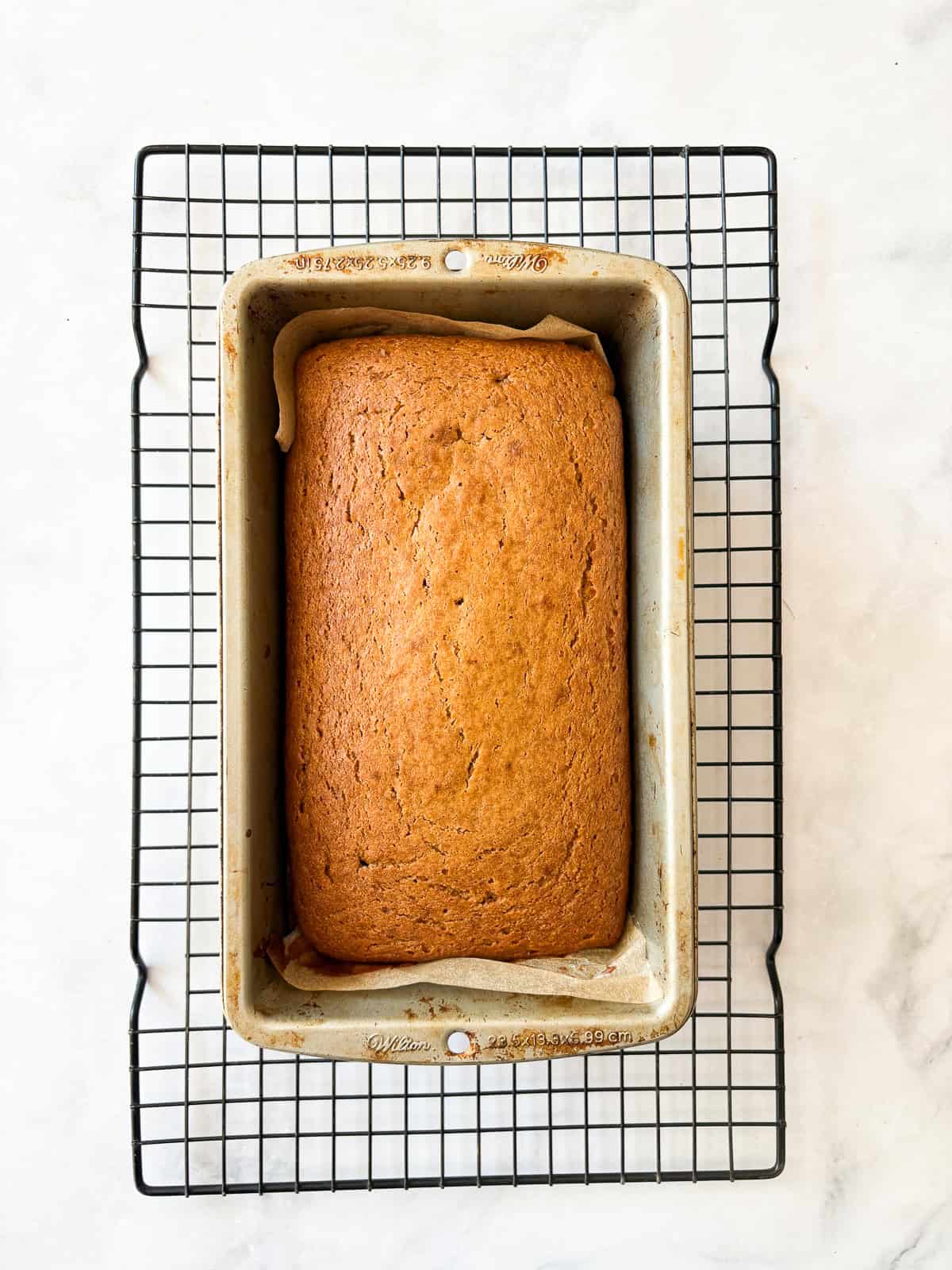 A loaf of oat flour pumpkin bread cools in the pan on a rack.