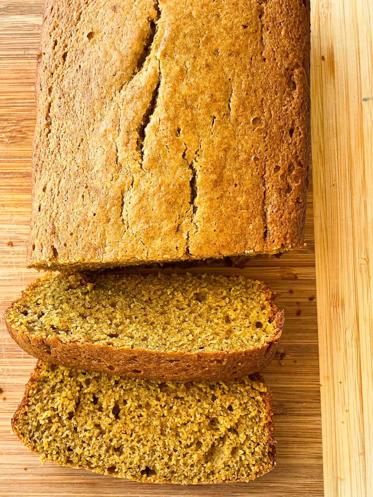 A few slices are cut from an oat flour pumpkin bread on a cutting board.