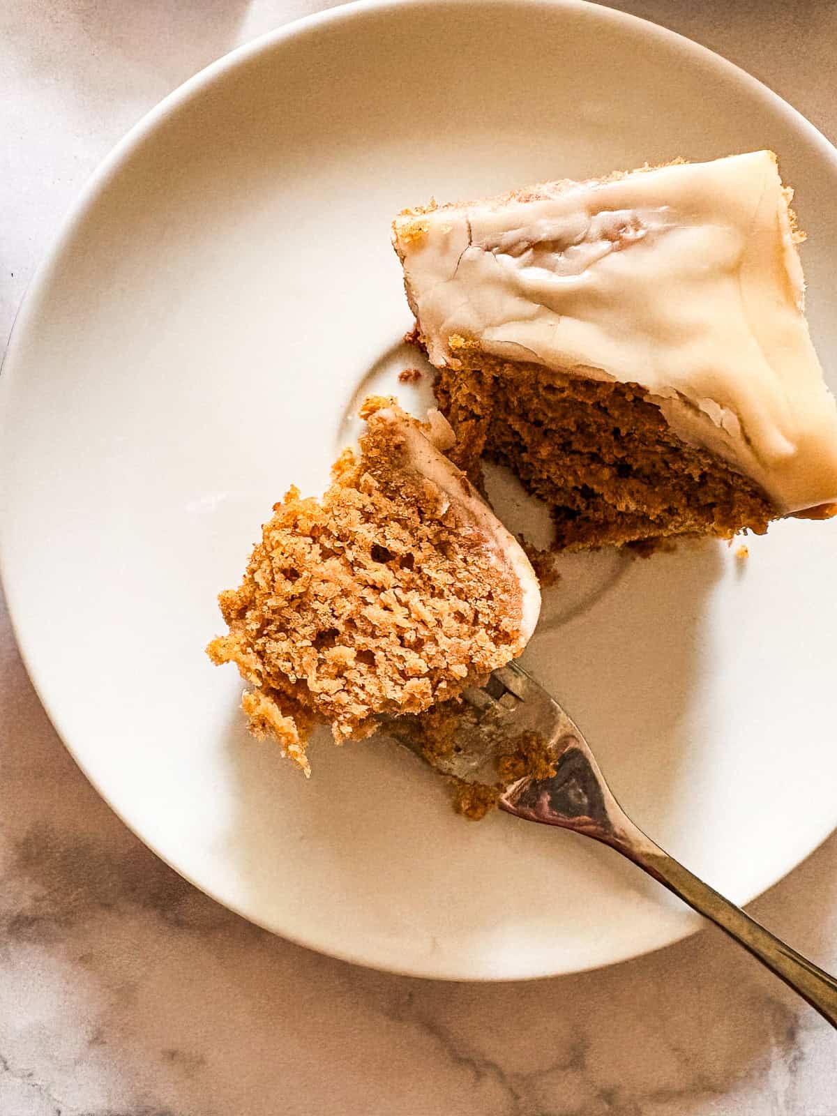 A soft, fluffy, and warmly spiced oat flour pumpkin cake that's topped with a slick of sweet maple glaze. Naturally gluten-free! A fork cuts into a piece of oat flour pumpkin cake to show the crumb.