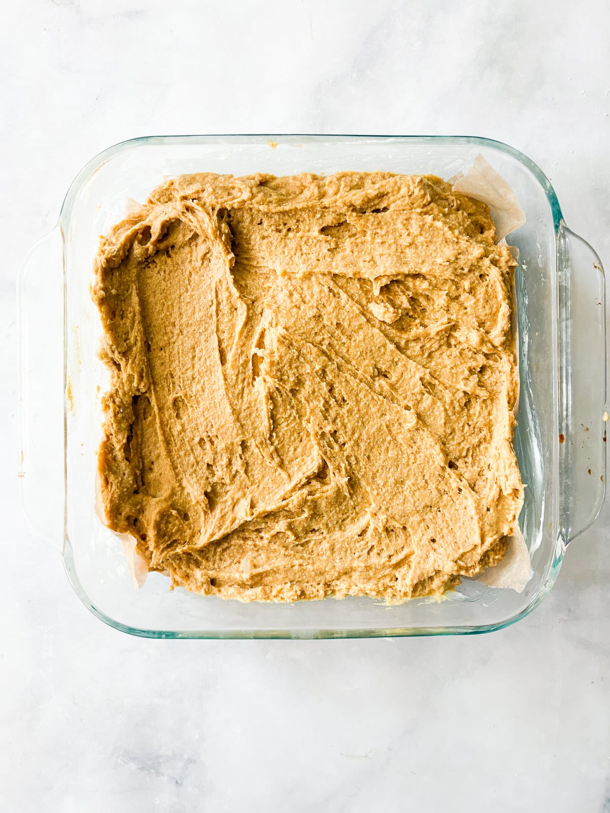 A soft, fluffy, and warmly spiced oat flour pumpkin cake that's topped with a slick of sweet maple glaze. Naturally gluten-free! Oat flour pumpkin cake batter in a baking dish.