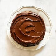 A gluten free dark chocolate cake with chocolate icing on a white plate.