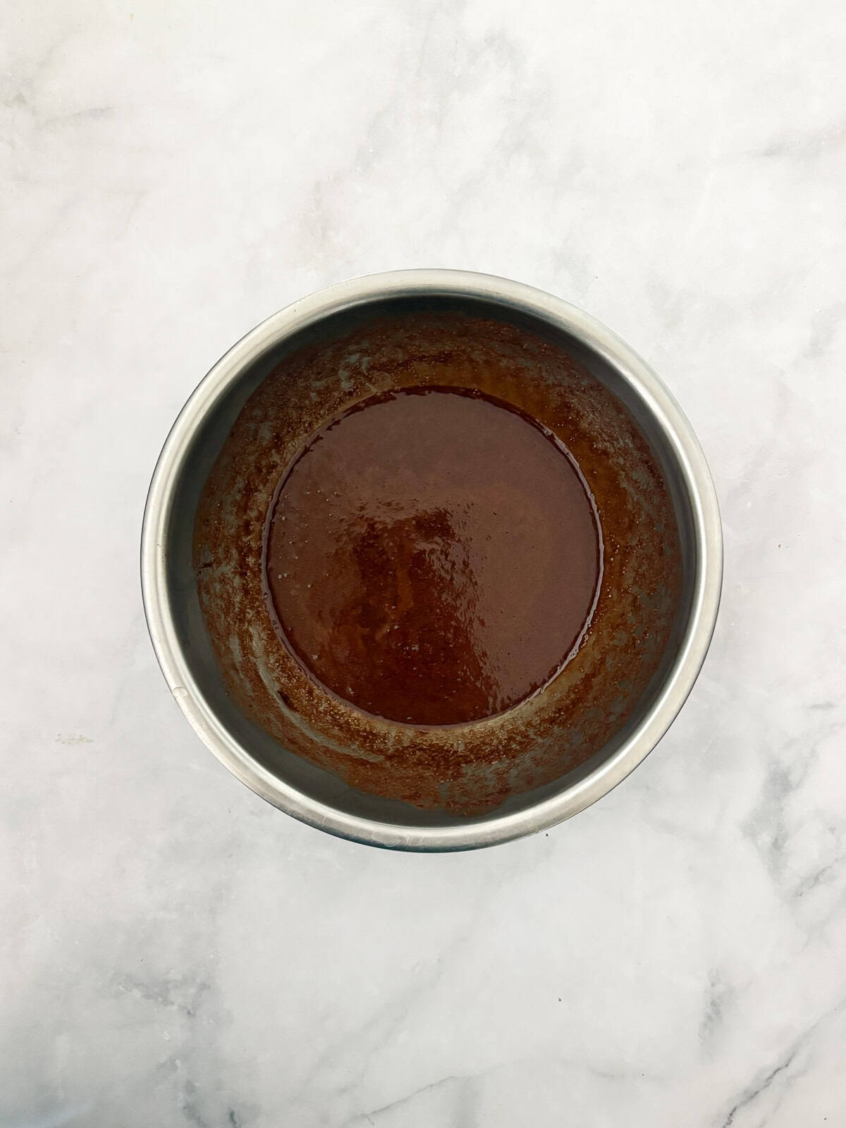 A tender, deeply dark gluten free chocolate olive oil cake capped with a layer of homemade chocolate icing. Chocolate icing in a bowl.