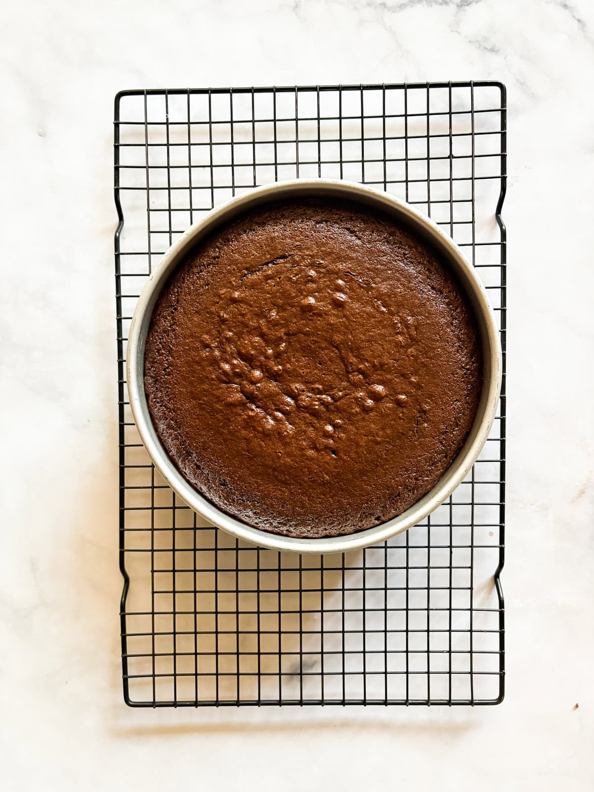 A tender, deeply dark gluten free chocolate olive oil cake capped with a layer of homemade chocolate icing. A gluten free chocolate olive oil cake cools in the pan.