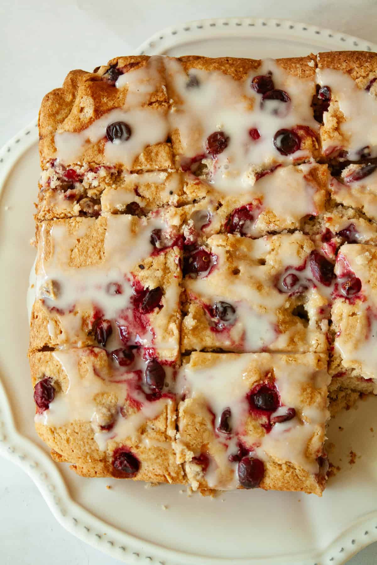 A gluten free cranberry cake cut into squares on a white plate.