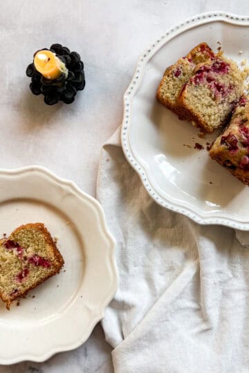 A candle burns next to slices of gluten free cranberry lemon loaf.